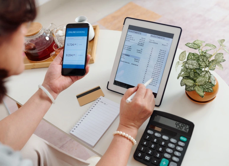 Person using a smartphone and tablet to manage online banking and investments, symbolizing digital financial management automation.